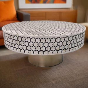 May include: A round, white coffee table with a black and white geometric pattern on the top. The table has a silver base.