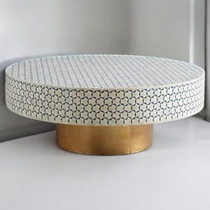 May include: A round, white coffee table with a geometric pattern in blue. The table has a gold base.