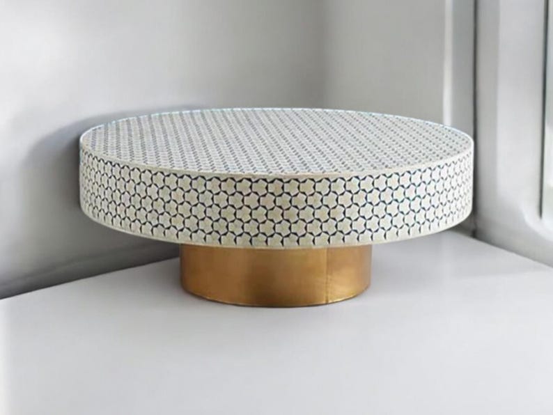 May include: A round, white coffee table with a geometric pattern in blue. The table has a gold base.