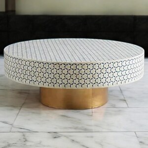May include: A round coffee table with a white and blue geometric pattern on the top and a gold base.