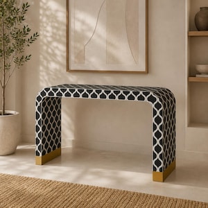 May include: A waterfall console table featuring a black and white geometric ogee pattern across its entire surface. The rectangular table has a continuous curved design and is finished with metallic gold-toned caps on both base ends.