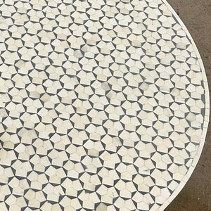 May include: A round table top with a geometric pattern of white and black bone inlay. The table top is made of bone and has a smooth, polished finish.