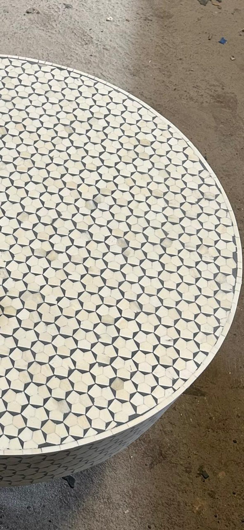 May include: A round table top with a geometric pattern of white and black bone inlay. The table top is made of bone and has a smooth, polished finish.
