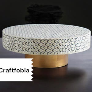 May include: A round, white coffee table with a geometric pattern and a gold base. The table is made of bone inlay and has a modern design.