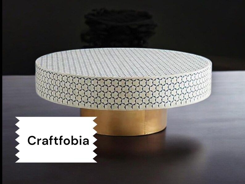 May include: A round, white coffee table with a geometric pattern and a gold base. The table is made of bone inlay and has a modern design.