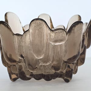 May include: A brown glass bowl with a unique, textured, wavy design. The bowl has a wide, shallow opening and a rounded base.