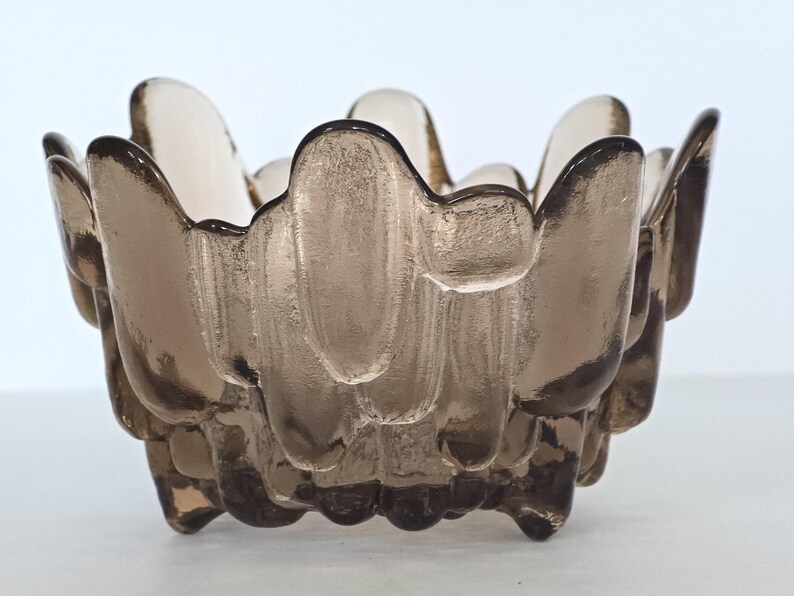 May include: A brown glass bowl with a unique, textured, wavy design. The bowl has a wide, shallow opening and a rounded base.
