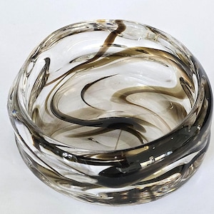 May include: A clear glass bowl with swirling brown and black patterns. The bowl has a rounded shape and a thick, textured rim. The design creates a sense of movement and depth.
