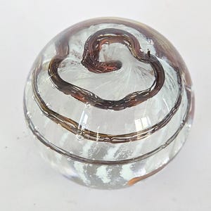 May include: A clear glass paperweight with brown and white swirls inside. The swirls are in a heart shape.