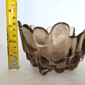 May include: A small, brown glass bowl with a unique, textured design. The bowl has a scalloped edge and appears to be handmade.