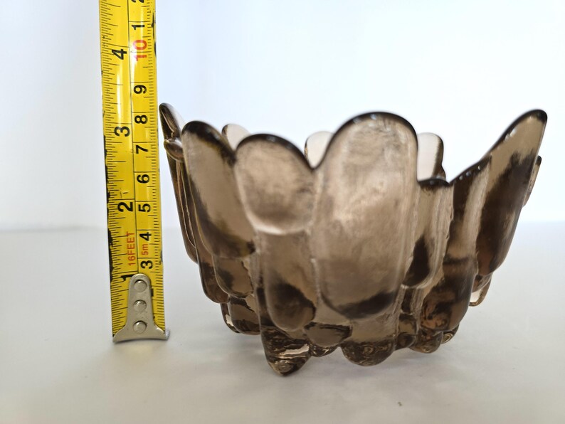 May include: A small, brown glass bowl with a unique, textured design. The bowl has a scalloped edge and appears to be handmade.