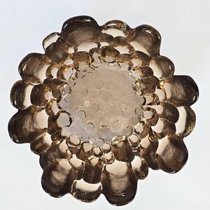 May include: A brown glass dish with a textured, bubble-like design. The dish is round and has a slightly raised rim.