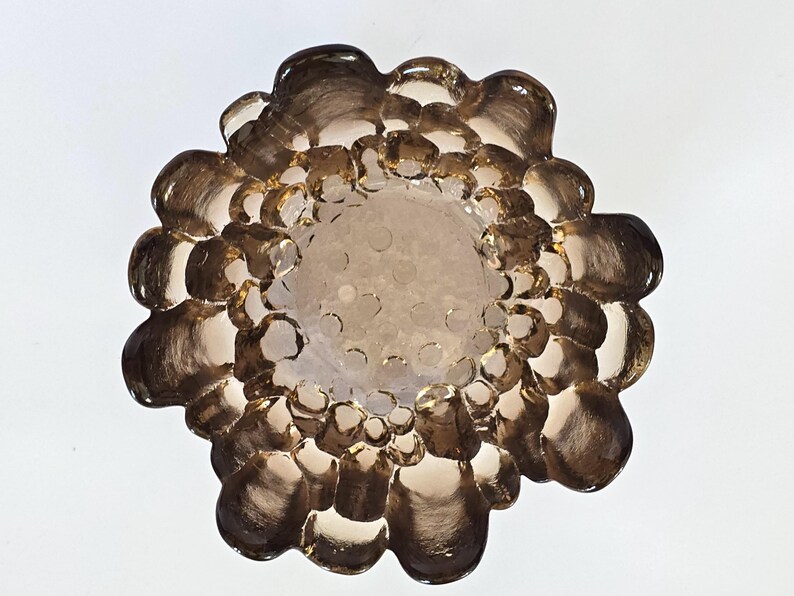 May include: A brown glass dish with a textured, bubble-like design. The dish is round and has a slightly raised rim.