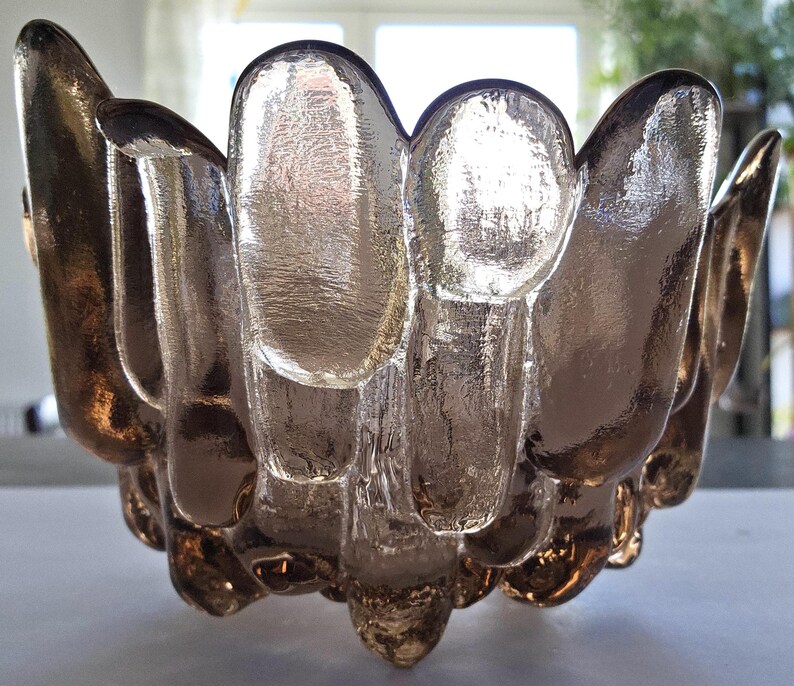 May include: A clear glass bowl with a unique, textured design. The bowl has a rounded shape and is made of thick glass. The glass has a slightly frosted appearance, giving it a vintage look.