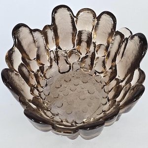 May include: A brown glass bowl with a unique, textured design. The bowl has a scalloped edge and a textured bottom.