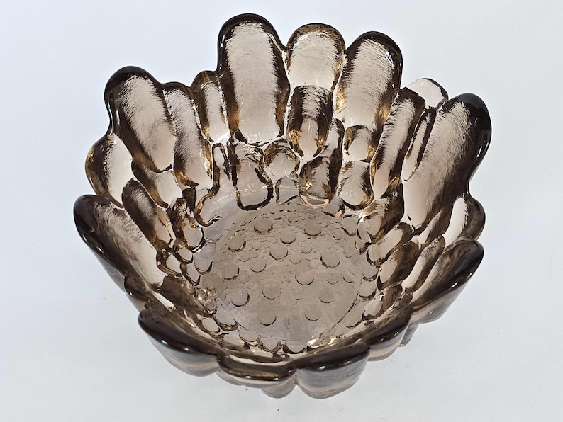 May include: A brown glass bowl with a unique, textured design. The bowl has a scalloped edge and a textured bottom.
