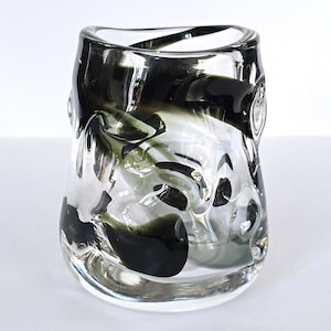 May include: A clear glass vase with a unique, textured design. The vase features dark gray and black swirls throughout the glass, creating an abstract pattern. The vase has a rounded shape and is suitable for displaying flowers or as a decorative piece.