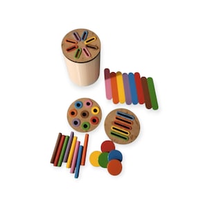 May include: Wooden educational toy set with a cylindrical sorter, two circular sorters, and colourful wooden shapes. Includes sticks, discs, and a set of colorful rectangular pieces. The toys are arranged on a white background.