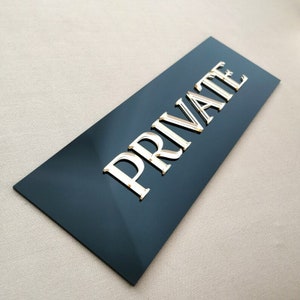 May include: A black rectangular sign with the word "PRIVATE" in raised gold letters.