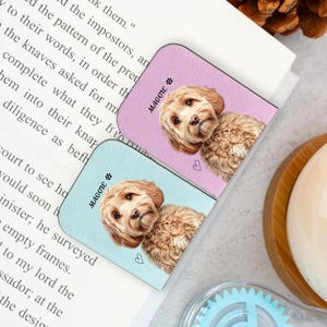 May include: Two dog-themed magnetic bookmarks. One is light blue, the other is lavender. Each features a realistic illustration of a fluffy, brown-haired dog, the name "Maggie", and a small heart.