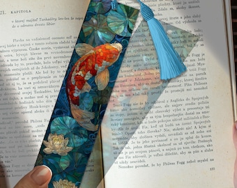 May include: A decorative bookmark featuring a koi fish design in shades of red, orange, and white, set against a blue background with lily pads. The bookmark has a blue tassel attached.