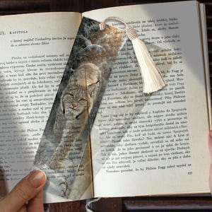 Pode incluir: Um marcador de livros com uma ilustração de lince e uma borla creme, colocado num livro. O texto é visível nas páginas do livro.