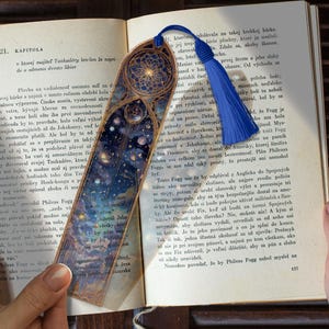 Puede incluir: Marcapáginas decorativo con borla azul. El marcapáginas presenta un diseño detallado de un cielo nocturno estrellado con detalles dorados, perfecto para los amantes de la lectura.