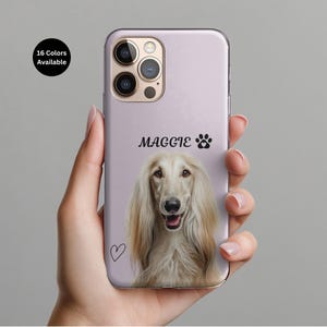 May include: A light purple phone case featuring a portrait of a dog with long, flowing, light-colored fur. The name "MAGGIE" and a paw print are above the dog's image. A heart is drawn on the lower left. The text "16 Colors Available" is in a black circle.