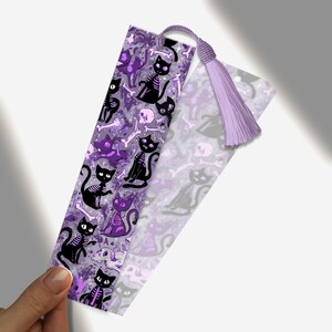 May include: A purple and black bookmark featuring a repeating pattern of skeleton cats, bones, and skulls. The bookmark has a matching purple tassel attached to the top. The design is whimsical and spooky.