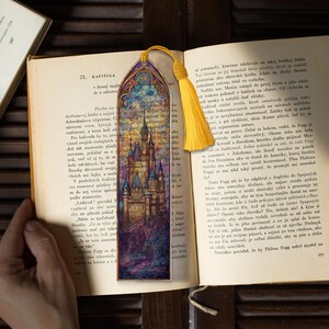 May include: A decorative bookmark with a castle design, featuring stained glass windows and a yellow tassel. The bookmark is placed in an open book, adding a touch of fantasy.