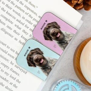 May include: Two rectangular dog-themed bookmarks. One is light blue, the other is pink. Each features a smiling dog portrait, the name "Maggie", and a paw print icon. A small heart is also visible on each bookmark.