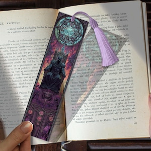 May include: A decorative bookmark with a purple tassel. The bookmark features a detailed illustration of a seated figure in dark armor, set against a background of a stained-glass window design.