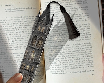 Puede incluir: Marcapáginas detallado con un diseño de edificio gótico, ventanas arqueadas y una borla. El marcapáginas está colocado sobre un libro abierto.