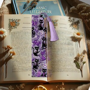 May include: A decorative bookmark featuring a repeating pattern of black cats with skeleton designs and purple cats on a light purple background. The bookmark has a lavender tassel and is placed in an open book with the title "CLASSIC LITERATURE" visible.