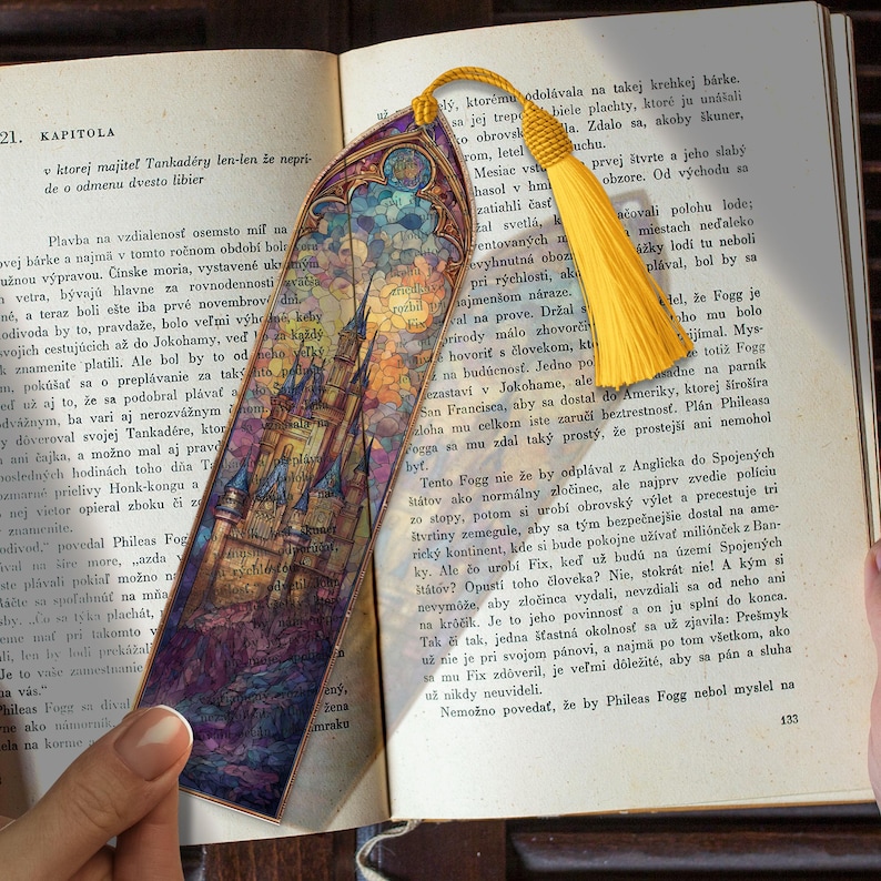 May include: A bookmark with a castle design in stained glass style, featuring blue, purple, and orange colours. It has a yellow tassel and is in an open book.