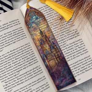 May include: A decorative bookmark featuring a castle design in a stained-glass style, with a yellow tassel. The bookmark is positioned on a book, adding to its aesthetic.