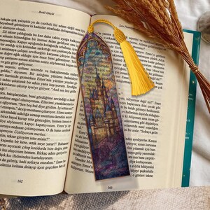 May include: A decorative bookmark featuring a castle illustration, a yellow tassel, and a patterned top. The bookmark is in an open book with text on the pages.
