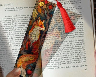 May include: A stained glass style bookmark featuring a fox in autumn colors. The bookmark has a red tassel and is set against the backdrop of an open book, perfect for book lovers.