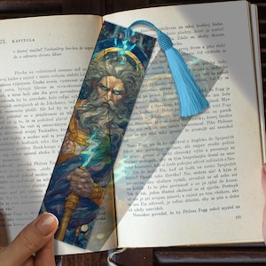 May include: A bookmark featuring a detailed illustration of a bearded man with a stern expression, possibly a depiction of a mythological figure. The bookmark has a blue tassel and is set against the backdrop of an open book.
