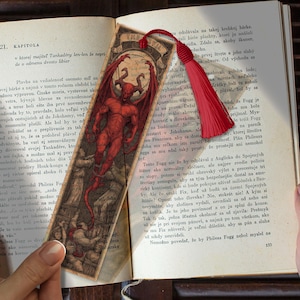 May include: A bookmark featuring a red devil illustration with horns and wings, with the text "THE DEVIL" at the top. A red tassel hangs from the top. The bookmark is placed in an open book.