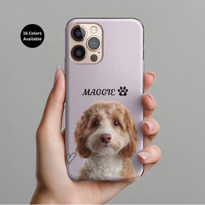 May include: A light purple phone case featuring a portrait of a dog with brown and white fur. The name "MAGGIE" is printed in black script above a paw print. A small heart is drawn on the lower left. The text "16 Colors Available" is in a black circle.
