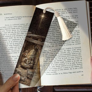 May include: A bookmark featuring a Nativity scene illustration with a bright star, set against a dark background. The bookmark has a cream-colored tassel and is placed in an open book.
