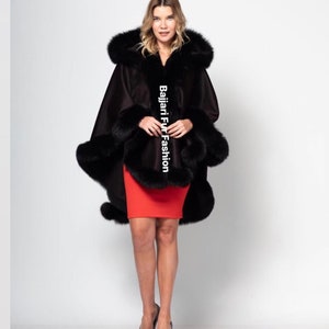 Puede incluir: Una capa negra con capucha y ribete de piel negra. La capa se lleva sobre una falda roja. El texto "Bajjari Fur Fashion" es visible en la capa.