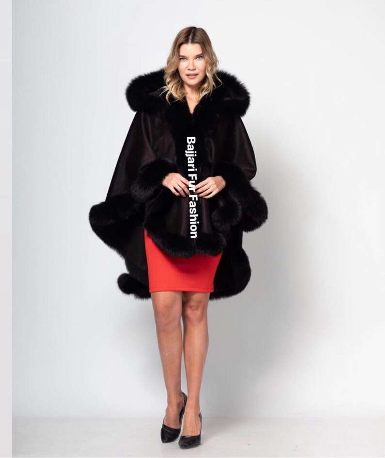 Puede incluir: Una capa negra con capucha y ribete de piel negra. La capa se lleva sobre una falda roja. El texto "Bajjari Fur Fashion" es visible en la capa.