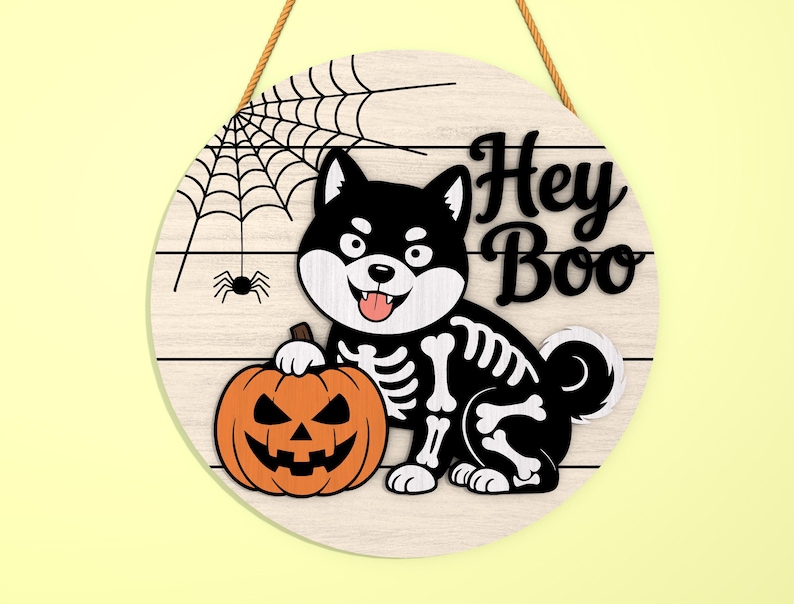 Może przedstawiać: Okrągły drewniany znak na Halloween z czarno-białym psem Shiba Inu w kostiumie szkieletu trzymającym pomarańczową dynię. Znak zawiera napis "Hey Boo" i wz&oacute;r pajęczyny.