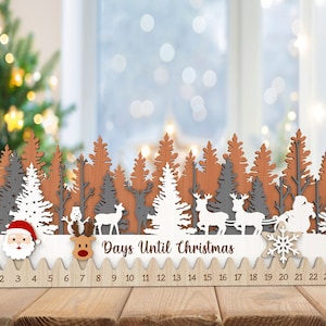 Può includere: Calendario dell'avvento in legno con una scena di foresta invernale. Il calendario presenta uno sfondo bianco con alberi marroni e grigi, un pupazzo di neve, renne e Babbo Natale. I numeri da 1 a 24 sono stampati nella parte inferiore del calendario.