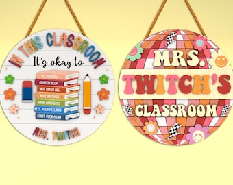 May include: Two round wooden signs with colorful designs. The first sign says "In this classroom it's okay to..." with a list of positive affirmations. The second sign says "Mrs. Twitch's Classroom" with a disco ball design.