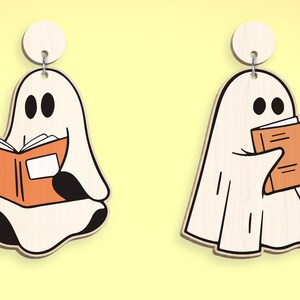Op de afbeelding: Twee witte spookversieringen met zwarte ogen. E&eacute;n spook houdt een oranje boek vast en de andere houdt een gesloten oranje boek vast.