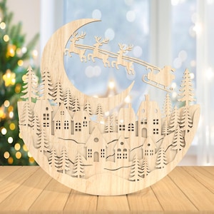 Peut inclure: Décoration de Noël en bois représentant le traîneau du Père Noël et ses rennes au-dessus d'un village. La décoration en bois sculpté comprend des maisons et des arbres. Posée sur une surface en bois.