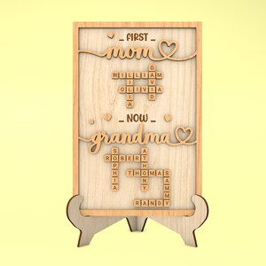 May include: Wooden sign with the words "FIRST MOM NOW GRANDMA" spelled out using Scrabble tiles. The sign is on a small wooden stand.